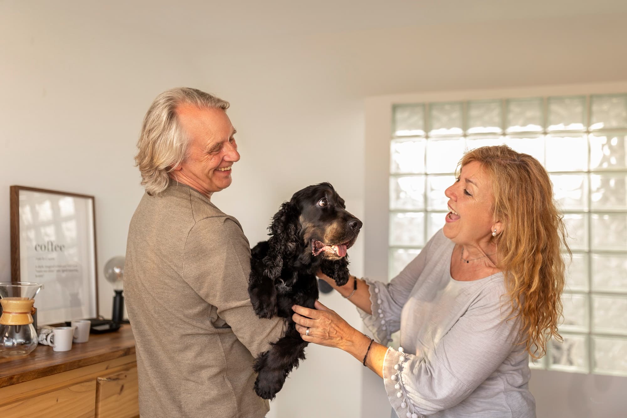 A couple holding up a black dog while smiling at each other.