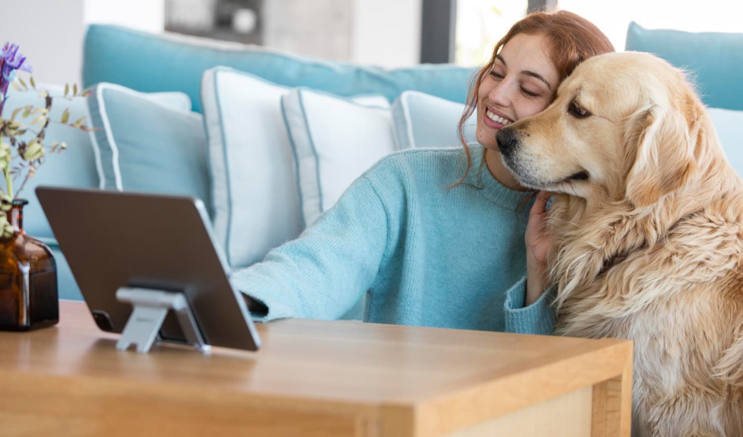 A women sitting at home with her dog as they look at her tablet.