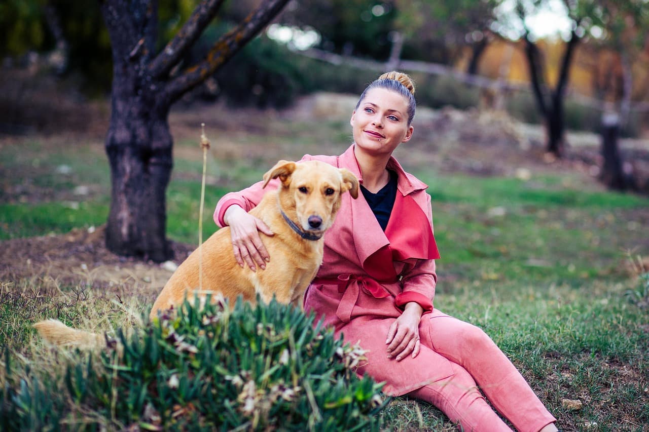 A girl in pink sitting with her dog in the park as they look into the distance.